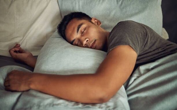Man sover lugnt på sidan i en säng med kuddar