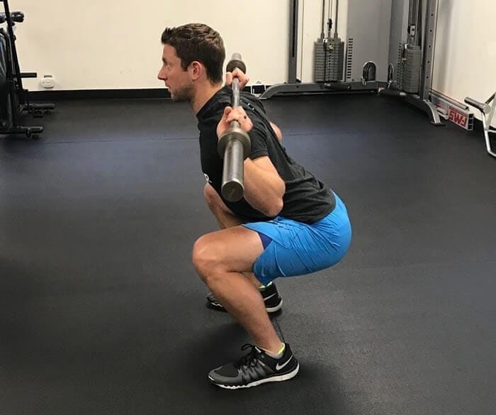 Man visar en knäböj med skivstång på axlarna i ett gym
